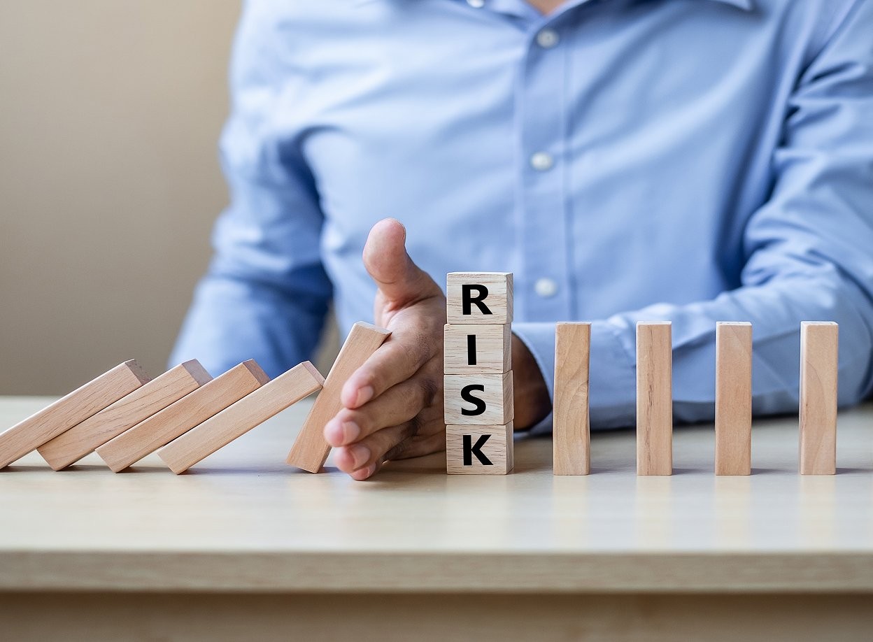 Hand stopping falling dominoes beside blocks spelling RISK, representing security risk management