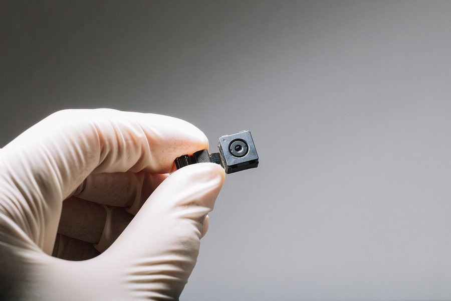 Gloved hand holding a miniature covert camera found during a TSCM sweep