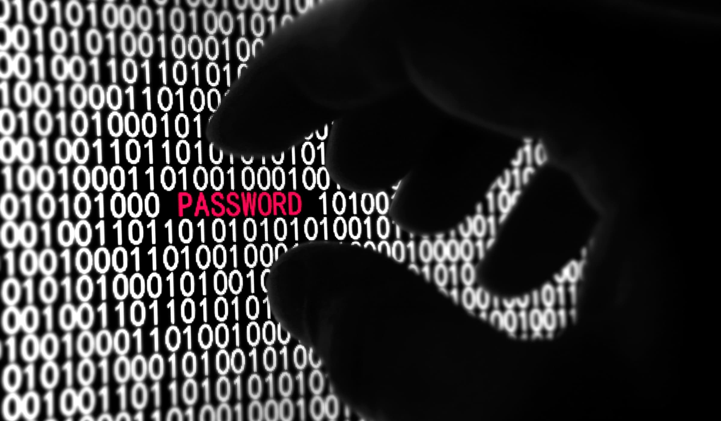 Silhouetted hand reaching for a password hidden in binary code, representing cyber security threats